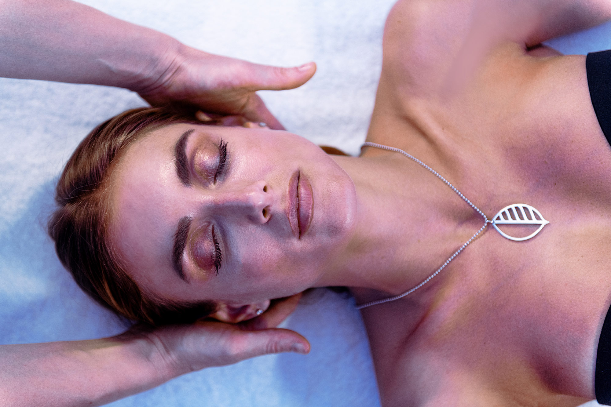 Relaxed woman receiving head massage, leaf necklace, serene atmosphere.